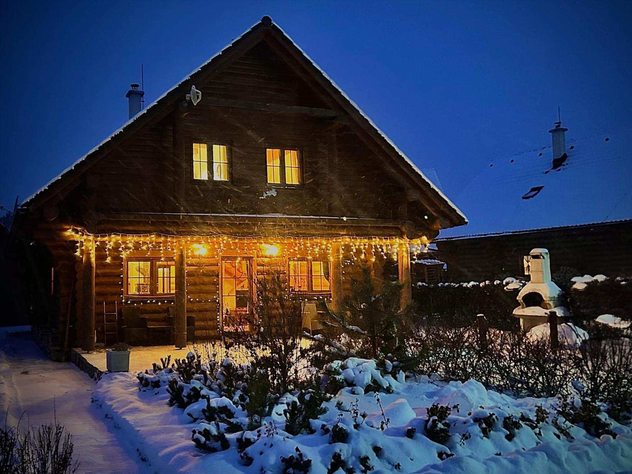 Blockhaus Bosorka Zrub an einem Winterabend mit beleuchteten Fenstern